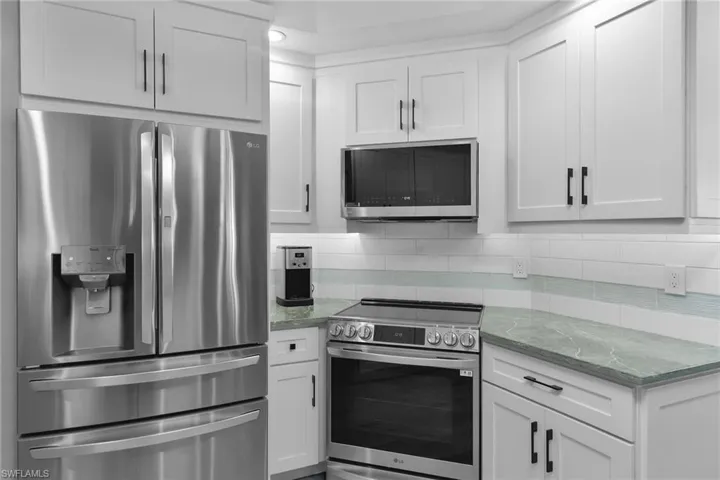 Kitchen featuring stainless steel appliances, light stone countertops, white cabinets, and backsplash
