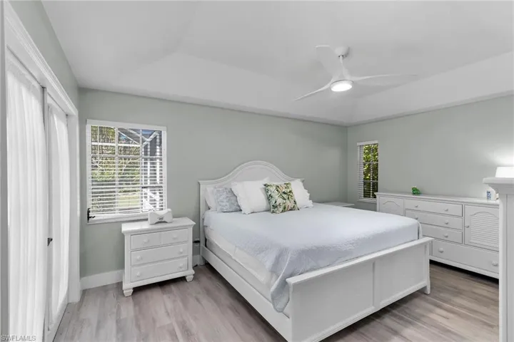 Bedroom with a raised ceiling, a ceiling fan, and light wood finished floors