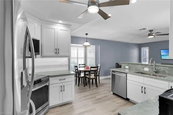 Kitchen with appliances with stainless steel finishes, backsplash, light stone countertops, white cabinets, and recessed lighting