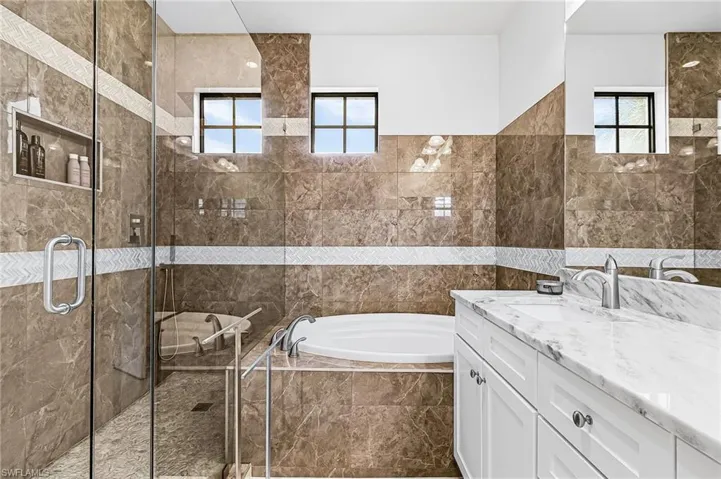 Bathroom featuring vanity, a bath, a shower stall, and tile walls