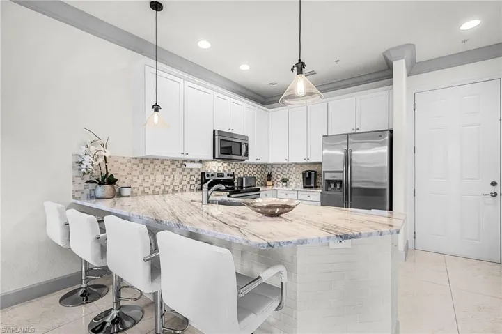 Kitchen with stainless steel appliances, a breakfast bar area, a peninsula, white cabinets, and decorative backsplash