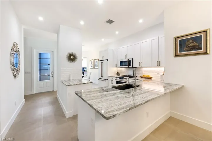 Kitchen featuring light stone counters, GE Cafe style appliances, and a peninsula style bar.