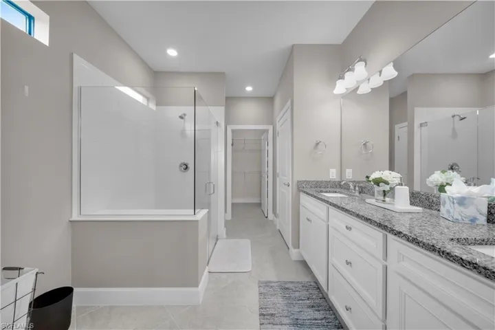 Spacious bathroom featuring a frameless glass shower enclosure, dual vanity with undermount sinks, stone countertops, and recessed lighting