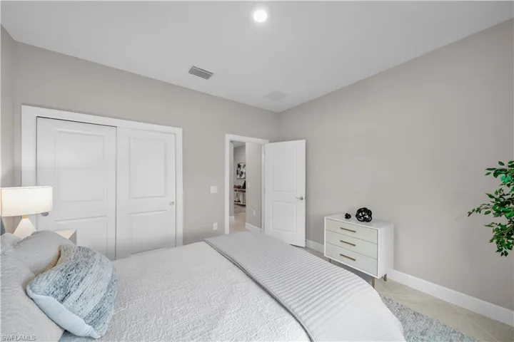Bedroom featuring neutral-toned walls, white trim, recessed lighting, and a closet with sliding panel doors