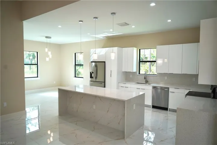 Kitchen featuring light stone counters, backsplash, light marble finish flooring, stainless steel appliances, and white cabinets
