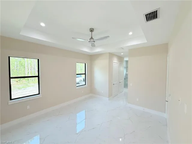 Spare room with light marble finish floors, a tray ceiling, recessed lighting, and a ceiling fan