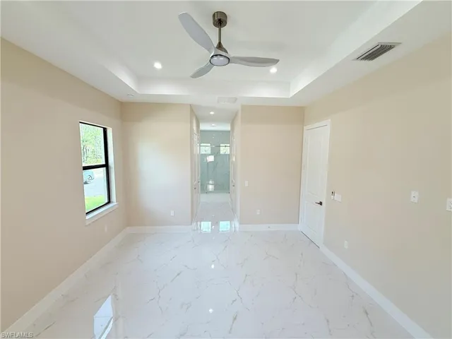 Empty room with a raised ceiling, light marble finish floors, recessed lighting, and ceiling fan