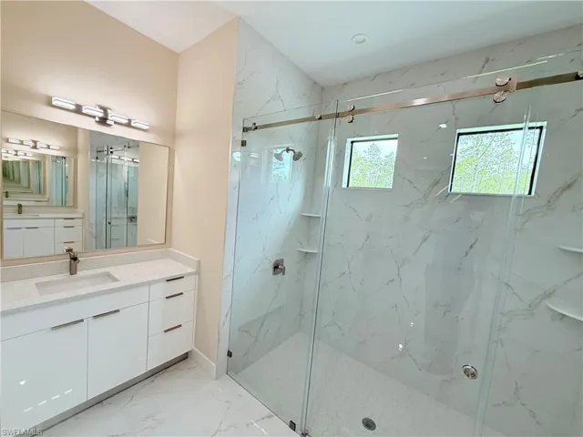 Bathroom featuring vanity, light marble finish flooring, and a marble finish shower