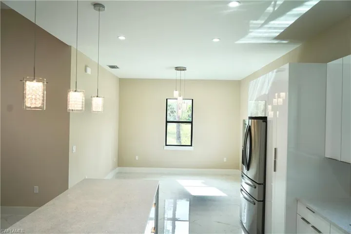 Kitchen featuring light marble finish floors, stainless steel refrigerator with ice dispenser, white cabinetry, hanging light fixtures, and light stone counters