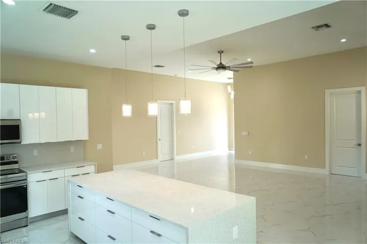 Kitchen with light marble finish floors, a kitchen island, appliances with stainless steel finishes, hanging light fixtures, and modern cabinets