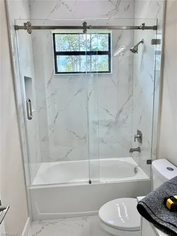 Bathroom with enclosed tub / shower combo, vanity, and marble look tiles