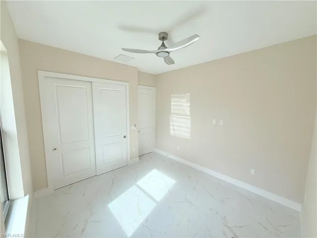 Unfurnished bedroom featuring marble look tile flooring, a closet, and ceiling fan