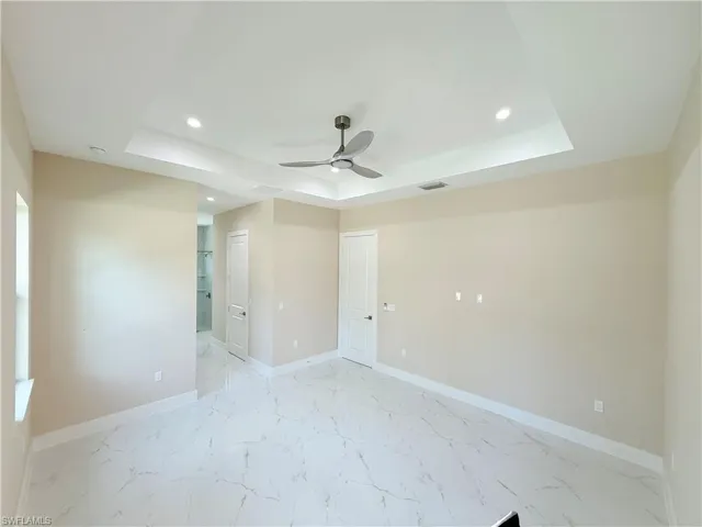 Spare room featuring a raised ceiling, recessed lighting, light marble finish flooring, and a ceiling fan
