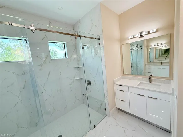 Bathroom featuring a marble finish shower, vanity, and light marble finish floors