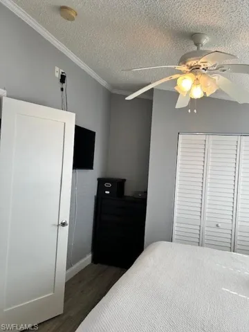 Bedroom with a textured ceiling, grey wood finished floors, crown molding, and ceiling fan