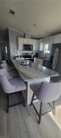 Kitchen featuring dark stone counters, a breakfast bar area, stove, white cabinetry, and a textured ceiling