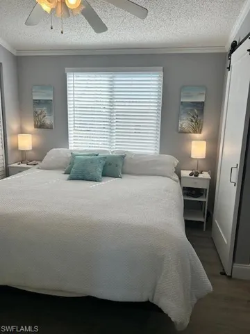 Bedroom with a barn door, crown molding, a textured ceiling, a ceiling fan, and multiple windows