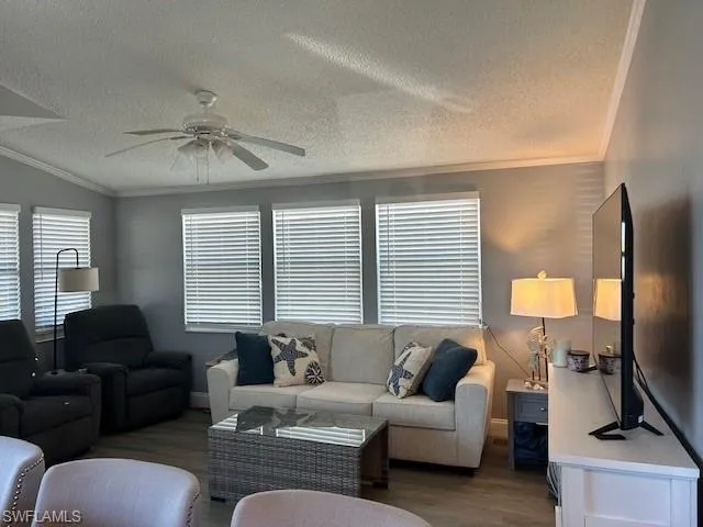 Living room featuring crown molding, wood finished floors, ceiling fan, and a textured ceiling