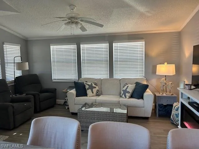 Living area featuring ceiling fan, crown molding, wood finished floors, and a textured ceiling