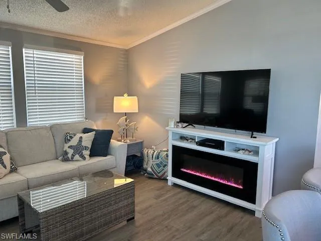 Living area featuring a textured ceiling, wood finished floors, ornamental molding, ceiling fan, and a glass covered fireplace