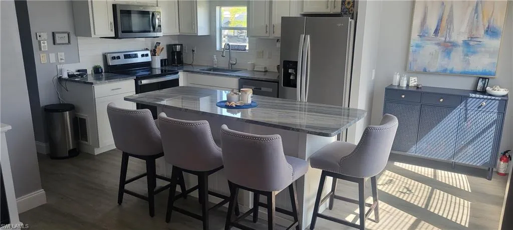 Kitchen featuring stainless steel appliances, white cabinets, a breakfast bar area, dark stone countertops, and tasteful backsplash