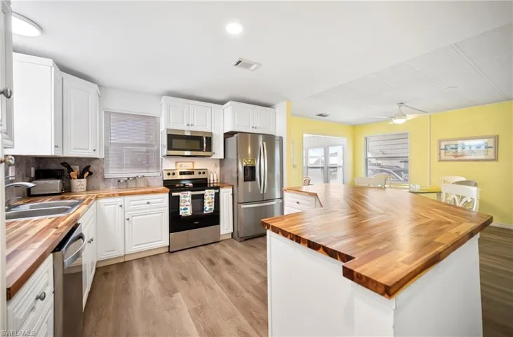 Kitchen with wood counters, white cabinetry, stainless steel appliances, light wood finished floors, and backsplash