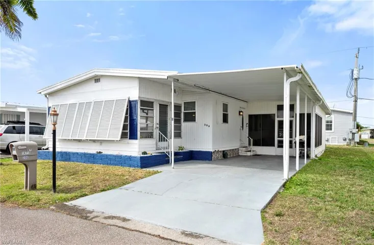 Manufactured / mobile home featuring a front lawn, entry steps, an attached carport, and driveway