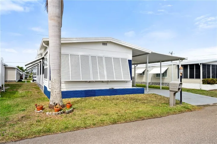 View of front of property with a carport, concrete driveway, a front lawn, and a sunroom