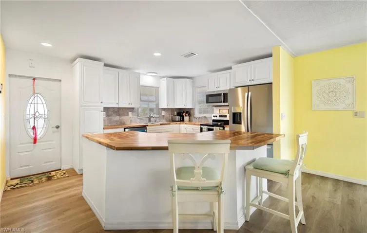 Kitchen featuring wooden counters, stainless steel appliances, white cabinets, a kitchen island, and tasteful backsplash