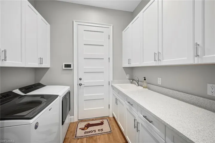 Laundry room featuring extensive white cabinetry, light-toned countertops, a utility sink, and wood-finish flooring