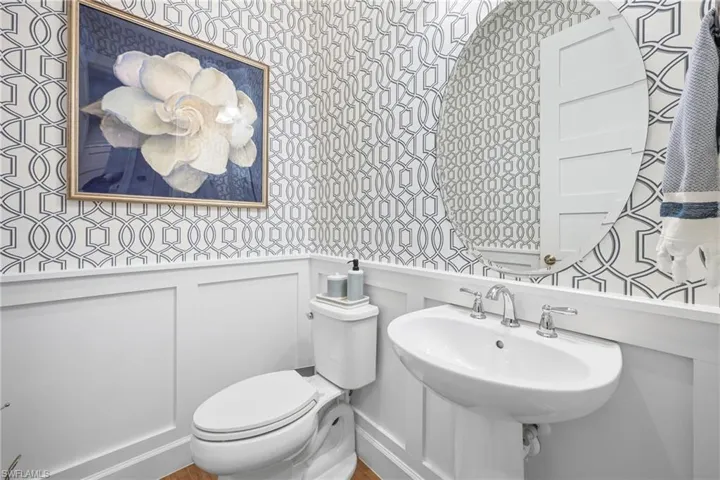 Pedestal sink with chrome faucet hardware, set against a geometric pattern wallpaper and white wainscoting