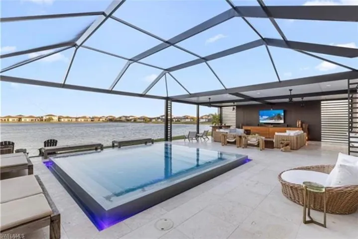 Expansive screened outdoor living area featuring a raised rectangular pool with integrated lighting, a water-facing entertainment wall with a mounted television, and a large tile patio