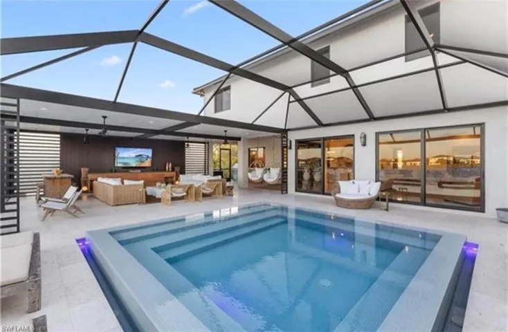 Screened outdoor living area featuring a rectangular pool with integrated steps, a covered patio, and large sliding glass doors providing access to the interior