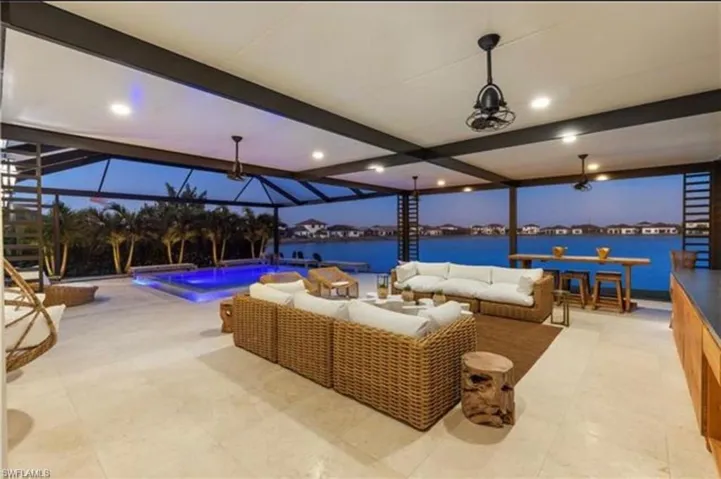 Expansive screened lanai featuring a private pool with ambient lighting, water frontage, an outdoor kitchen with integrated cabinetry, and multiple ceiling fans