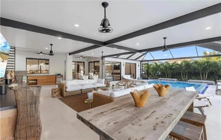 Expansive covered outdoor living area featuring a swimming pool, multiple ceiling fans, and a built-in outdoor kitchen with wood-finish cabinetry