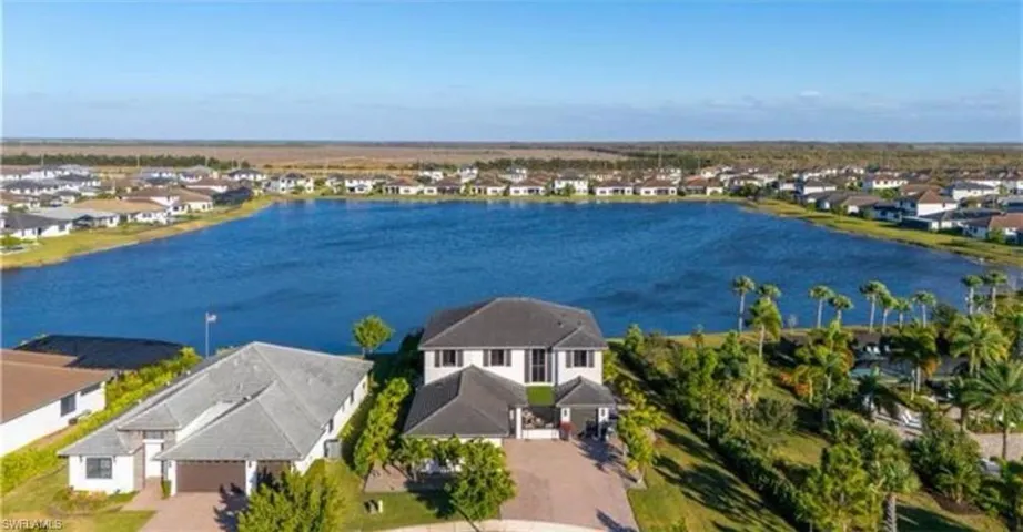 Expansive lakefront property featuring a two-story residence with a multi-car driveway, lush landscaping, and a broad water body