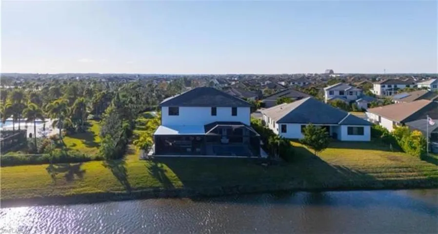 Waterfront property featuring a two-story residence with a screened lanai, an expansive lawn, and mature landscaping