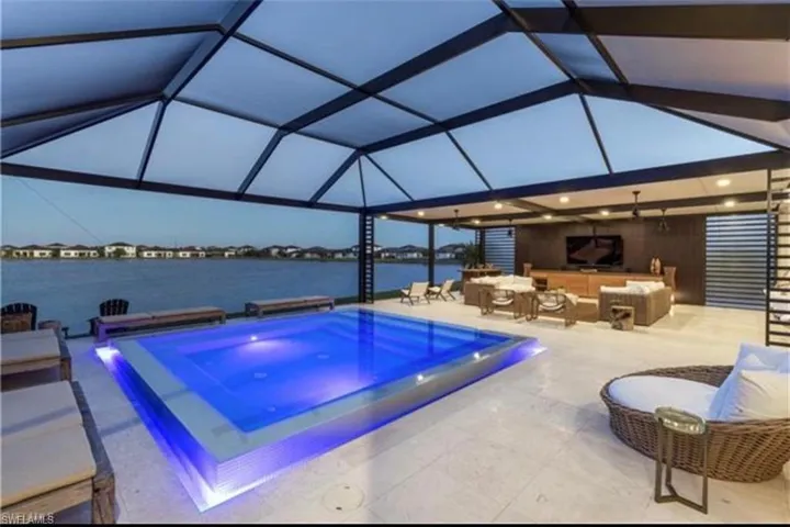Covered outdoor living space featuring an illuminated pool with integrated spa