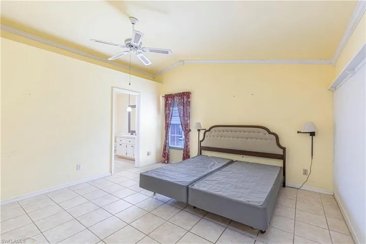 Bedroom with ornamental molding, light tile patterned flooring, baseboards, a ceiling fan, and ensuite bath