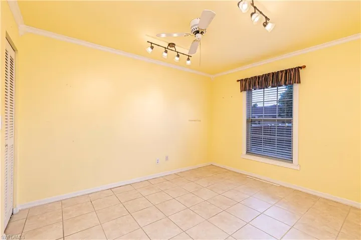 Spare room featuring crown molding, track lighting, a ceiling fan, light tile patterned floors, and baseboards