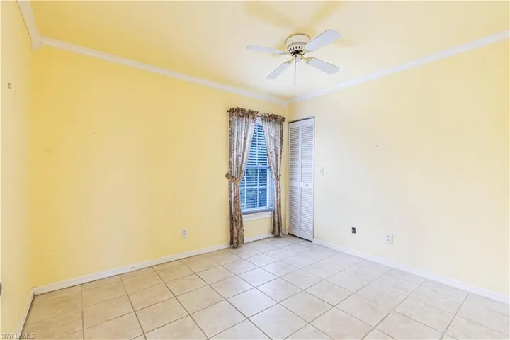 Empty room featuring crown molding, a ceiling fan, light tile patterned floors, and baseboards