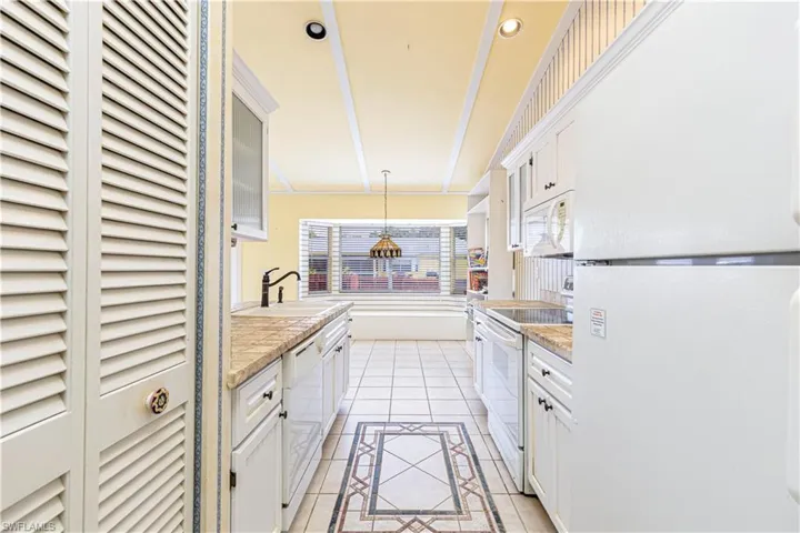 Kitchen featuring white appliances, a sink, light tile patterned floors, white cabinets, and recessed lighting