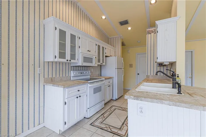 Kitchen featuring white appliances, a sink, light tile patterned floors, glass insert cabinets, and ornamental molding