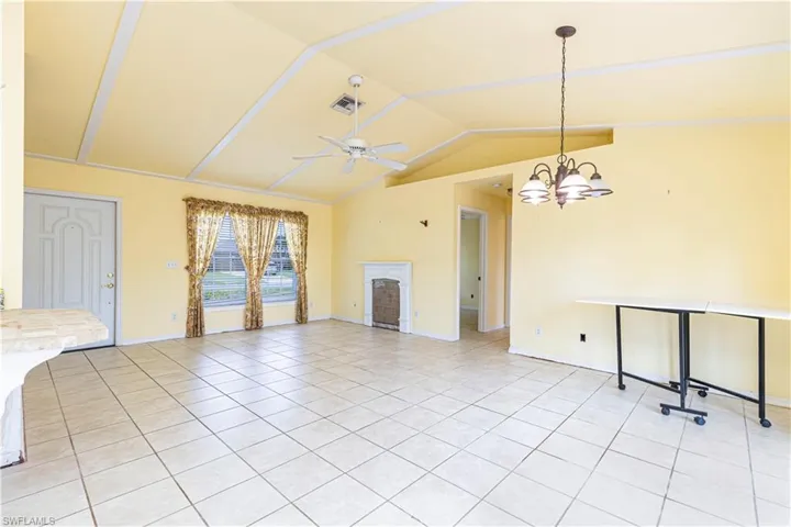 Unfurnished living room featuring light tile patterned floors, vaulted ceiling, ceiling fan, baseboards, and a fireplace