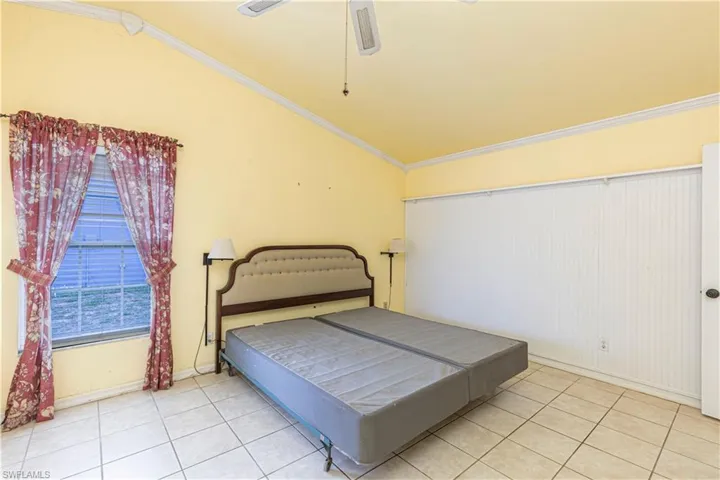 Bedroom featuring vaulted ceiling, light tile patterned flooring, crown molding, ceiling fan, and baseboards