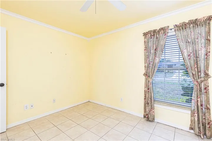 Spare room with crown molding, light tile patterned flooring, a ceiling fan, and baseboards