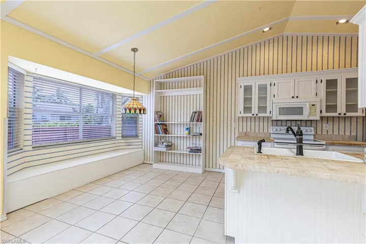 Kitchen featuring white appliances, vaulted ceiling, glass insert cabinets, light tile patterned flooring, and decorative light fixtures