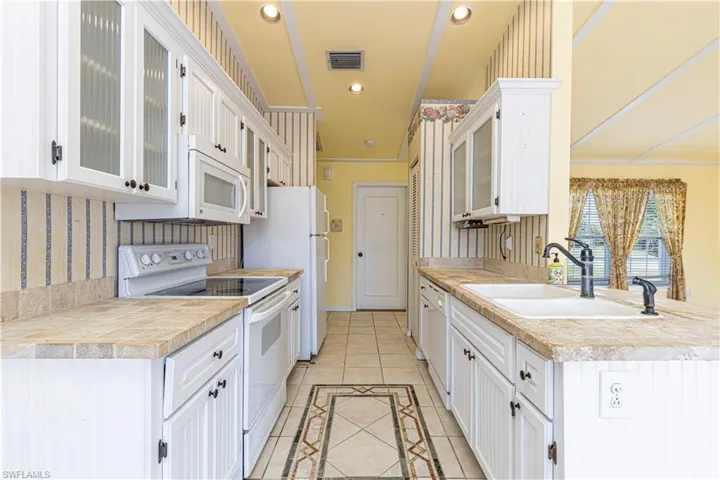 Kitchen featuring white appliances, light tile patterned floors, white cabinets, a sink, and glass insert cabinets