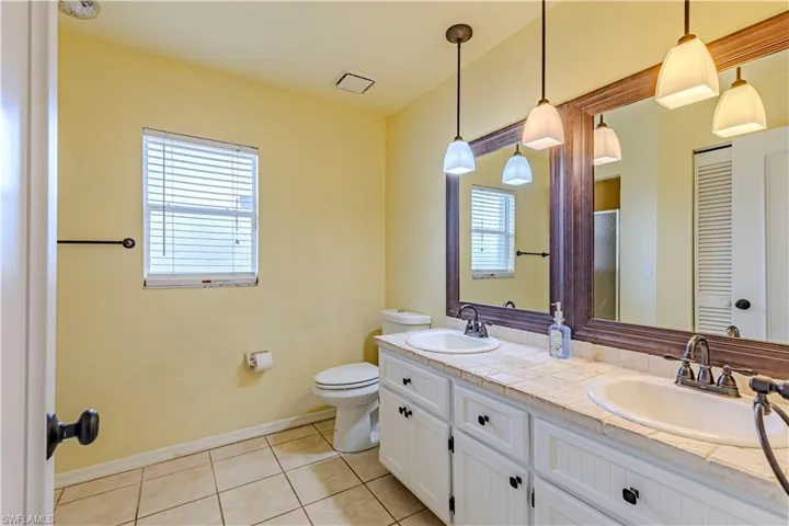 Full bathroom featuring toilet, tile patterned flooring, double vanity, and baseboards