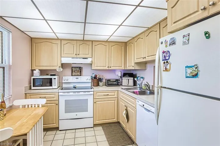 Kitchen with white appliances, light wood finish cabinetry, light tile patterned floors, a paneled ceiling, and healthy amount of natural light